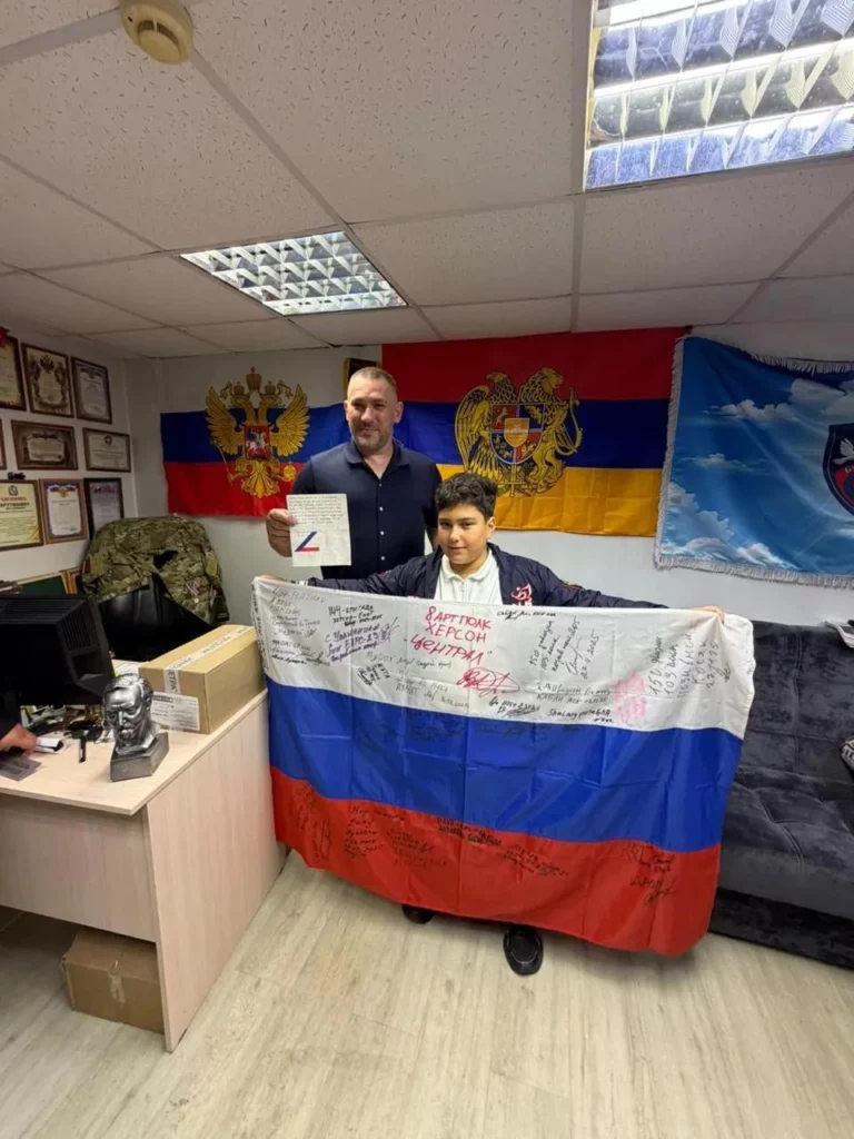 Юный волонтер Андрей Гаспарян с подаренным российским флагом с подписями бойцов