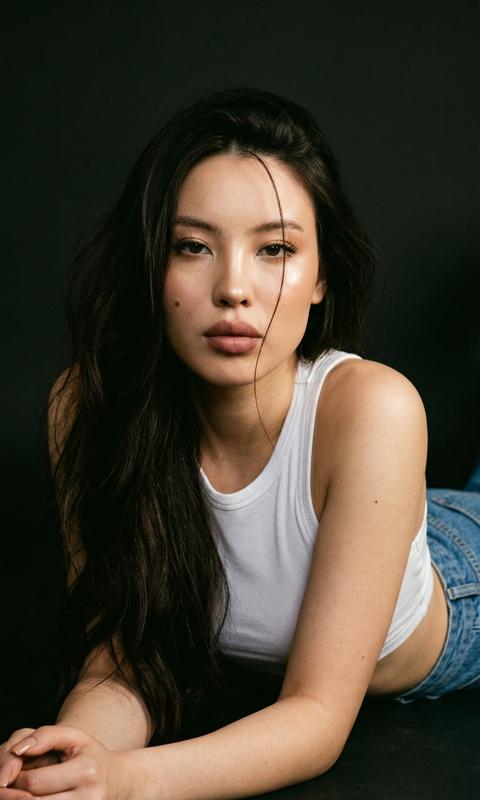 Создай крупный портрет, не меняя черты лица. Без ретуши. Вертикальный формат 9:16, 4К. Эффект плёночного кадра - съёмка винтажной камерой Kodak: мягкий тёплый направленный свет спереди, лёгкая зернистость, естественный контраст, глубокие мягкие тени, деликатный винтажный оттенок. Плотный fashion-портрет по плечи: девушка лежит на животе, корпус развернут к камере, плечи слегка приподняты, подбородок чуть опущен. Одежда: белый кроп-топ, голубые джинсы с высокой талией. Волосы распущенные, обьемные , одна тонкая прядь падает на лицо.
Безупречный макияж:хайлайтер во внутренних уголках глаз и на скулах, живая сияющая кожа. Розово-коричневые губы. Ногти нюдовые, форма квадрат. Фон тёмный, без деталей.