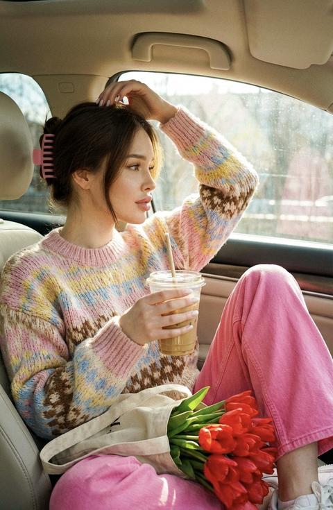 Кинематографический эффект с добавлением зерна
близкий кадр девушки  
Не меняй черты лица 
Качество 8К
Формат 9:16
Она сидит в машине на переднем пассажирском сиденье. Машина светлая, за окном солнечный день
Она одета в ярко розовые широкие джинсы, в вязаный свитер с рисунком (цвета розовый, желтый, голубой, коричневый, молочный цвета нежные) 
Волосы собраны розовым крабиком 
Белые кроссовки 
Она сидит одну ногу согнула в колено на сидение, в руках держит холодный кофе в прозрачном стакане со льдом, другой поправляет волосы, смотрит в окно лобовое.
На колене у нее лежит шоппер светлый и в нем букет алых тюльпанов 
Дневное освещение