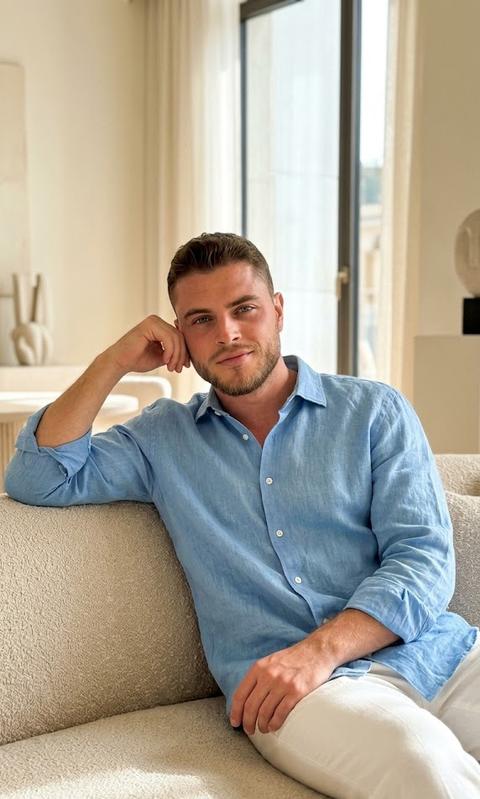 Create a portrait, without altering the facial features. Highly realistic photo, shot on iPhone 17 Pro Max in portrait mode. Aesthetic of modern "expensive" Instagram, "Old Money" style, and minimalism. Man in a loose blue linen shirt, and loose white trousers. Sitting on a beige sofa. He looks into the camera with a subtle smile.
The color palette is warm, pastel, in beige and cream tones.
Sitting in a relaxed pose, on a light sofa, leaning on his arm. Face turned three-quarters, gaze directed at the camera.
Soft natural lighting (daylight from a large window) that delicately highlights the contours of the face. Shadows are deep but soft. A light "cinematic" filter applied with a slight grain, characteristic of high-quality mobile photography. Atmosphere of comfort, quiet luxury, and serenity.