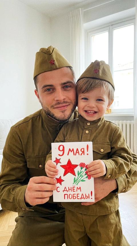 Создай изображение,сохрани внешность и черты лица
На фотографии мужчина и его ребенок  в советской форме, улыбаются, держа в руках открытку на 9 мая которую сделал сам. Стоит на фоне светлой комнаты. Они стоят рядом обнявшись, выражение лица искренне радостное. В стиле raw зернистость. Этот снимок передаёт атмосферу радости и предвкушения праздников, акцентируя внимание на семейных моментах.
Формат 9:16
Отец улыбается легкой улыбкой