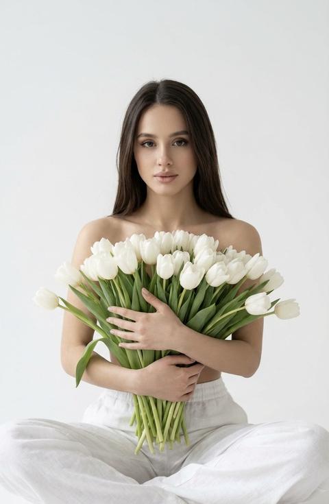 Создай крупный  фотопортрет , не меняя черты лица, молодой девушки с  прямыми  волосами, сидящей в позе лотоса на белом фоне. Безупречный нежный макияж. Она держит в руках огромную охапку белых тюльпанов, которые закрывают часть её тела. На ней свободные белые брюки. Минималистичный стиль, мягкое естественное освещение, пастельные тона, высокая детализация текстуры кожи и ткани. Эстетика чистоты, нежности и весны. Белый студийный фон, мягкий рассеянный свет, кинематографичное качество, 8k, фотореализм.