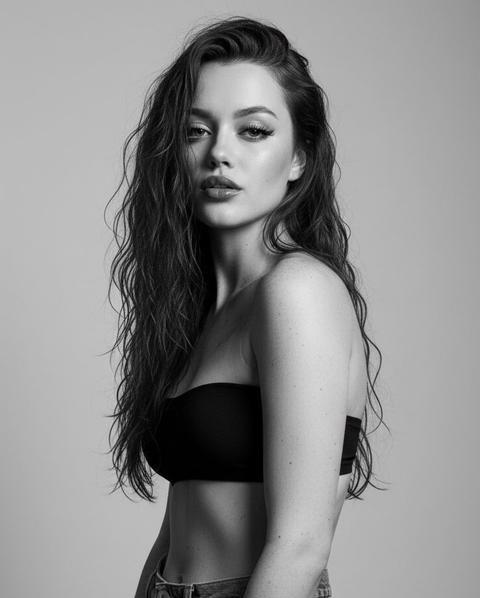 Художественная черно-белая фотография женщины. Крупный план, полупрофиль, она смотрит в камеру. На ней свободные джинсы с широкими штанинами в винтажном стиле, черный бюстгальтер без бретелек. Ее кожа/тело выглядят грязными, грубыми и неприкрашенными, что создает необузданный образ бунтарки. У нее длинные, влажные и взъерошенные волосы, которые беспорядочно падают на лицо и плечи. Фон простой, светло-серый, в стиле минимализма.
Изображение выполнено в высококонтрастных черно-/ белых тонах; резкое освещение подчеркивает контуры, тени и текстуру ее кожи. Общее впечатление - чувственное, смелое, провокационное и художественное - как от бунтарского журнала мод. Ее макияж поражает воображение: длинные, безупречная кожа и пухлые губы с коричневым блеском и темно-коричневой подводкой. У нее черные ногти квадратной формы. Перенеси внешность в точности как на референсе.