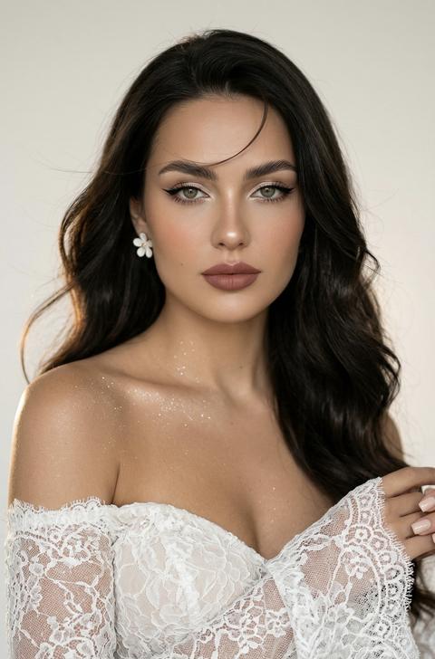 Create a close-up portrait, without altering facial features. The photo captures a young woman in a close-up, posing for a portrait. The shot highlights her well-groomed appearance and stylish look. She stands straight, perfectly centered.

Face and expression:
• Eyes: brightly accentuated with makeup. Shimmering beige eyeshadow is applied to the upper eyelids, complemented by sharp, long black winged eyeliner ("cat eye"). Eyelashes are fanned out.
• Eyebrows: Thick, brushed upwards (lamination effect), which gives the face a modern and open look.
• Skin: Skin tone is even, with a light tan, and a delicate peach blush on the cheekbones. The tip of the nose and cheekbones are subtly highlighted with a highlighter to give the face a glow.
• Lips: Full, expressive, painted with matte lipstick in a rose-brown shade. The upper lip has a clear contour.

Nude, square manicure.

Hair is long, wavy, shiny, blown by a light breeze, with one strand near the face. She has delicate, airy flower-shaped earrings.

The woman is wearing a lace, off-the-shoulder dress with long sleeves flared at the bottom, a fitted wedding dress. Her shoulders are covered with shimmer.

The background is light. Soft directional lighting from the left casts gentle highlights on her forehead, nose, and collarbones, with subtle shadows under her cheekbones. Hair is straight, peach top. The background has soft warm backlighting behind the girl. The image is shot at eye level with a shallow depth of field, ensuring the subject is sharp and natural skin tones are preserved without visible post-processing artifacts. 9:16. She stands straight, facing directly towards the camera.
