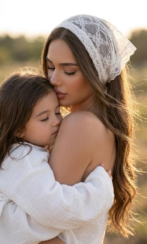 Create a close-up portrait, without changing facial features. Ultralistic outdoor portrait "golden hour," Flawless makeup, dusty rose colored lips. Close-up detailed portrait. Woman kissing a child's head. Child held tightly against the mother, eyes closed, Child wearing an oversized, very loose white muslin shirt, the woman wearing a white lace headscarf tied at the back of her head. Long hair completely down, soft airy strands falling on her back and beautifully fluttering in the wind. Skin with a light tan,