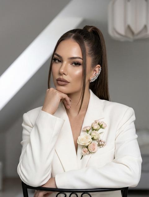 Создай портрет, не меняя черты лица. Фото выполнено в стиле Vogue, с добавлением чёткости и элегантности, создавая атмосферу высокой моды. Девушка сидит на черном железном стуле, её поза расслабленная, но с выраженной уверенностью. Стул наоборот Она  облокотилась на руку. 
Eë взгляд сосредоточенный, уверенный,
И
прямой, что добавляет глины и
эмоциональности снимку. Камера настроена на резкость и чёткость, идеально захватывая каждую деталь её образа.
Она носит молочный  костюм оверсайз,
состоящий из пиджака и брюк, на пиджаке нежно кремовые нежно розовые живые цветы пришиты или заколоты.
Кожа с лёгким загаром
Волосы собраны в высокий хвост гладкий 
Макияж выполнен в нюдовых тонах с тонкими чёрными стрелками, пышными / ресницами и матовыми нежно коричневыми губами , подчёркнутым хайлайтером для естественного сияния кожи.
Снимок сделан с использованием качественной камеры, что позволяет чётко видеть каждую деталь, текстуру костюма и макияжа  локоны у лица прямые
На ухе серьга манжета обьемная серебряная Освещение мягкое и направленное, с акцентом на ее лицо и украшения, создавая контраст между её и минималистичным светлым фоном.
9:16