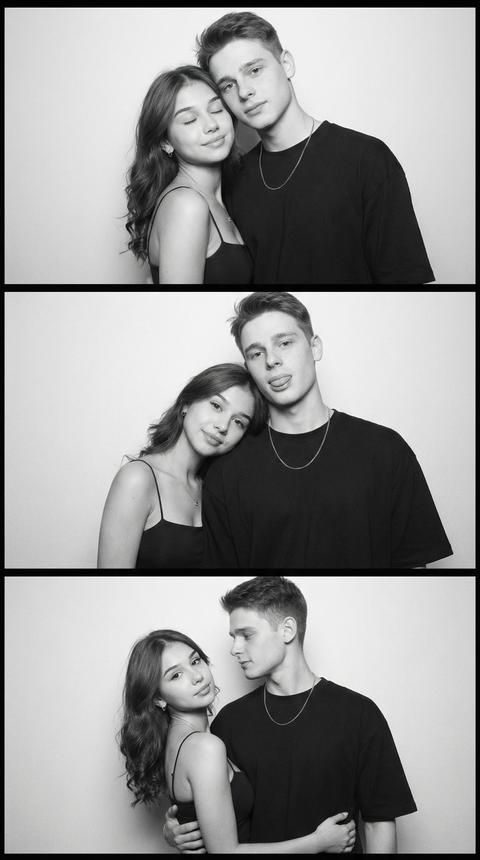 A vertical collage of three horizontal panels in a photo booth format. The image depicts a man and a woman posing in a studio black-and-white shoot. The sequence of shots conveys changing emotions and intimacy, while the location and angle are preserved. Faces from the uploaded photos must not be changed.

**In the top panel**, the man and woman stand close to each other, their bodies facing forward. The woman slightly tilts her head toward the man, her eyes closed, her lips in a soft smile. The man leans forward, their shoulders touching. Medium shot, chest-high.

**In the middle panel**, the woman tilts her head and rests it on the man's shoulder, her body facing forward, her gaze directed at the camera. The man looks into the lens and slightly sticks out his tongue, his pose relaxed, their shoulders touching. Medium shot, chest-high.

**In the bottom panel**, the man has his arm around the woman's waist. The woman's body is slightly turned three-quarters, her head tilted to the side, looking at the camera. The man is looking at her from the side, his head turned toward her, her pose more dynamic and lively. Medium shot, head-to-waist.

The woman's makeup features an even, natural skin tone, soft eyeshadow, accentuated lashes, and lips with a smooth, satin finish. Her hair has a soft, natural texture and is slightly casual, with a natural parting.

The outfit is casual and minimalist: the woman wears a dark top with thin straps, the fabric smooth and matte, and the man wears a dark, oversized T-shirt with a thin chain around his neck, without any additional accessories.

The shoot takes place against a neutral, light background in a studio photo booth.

The lighting is soft, frontal, and even, without harsh shadows. The light is flat and typical of a photo booth. The contrast is moderate, highlighting skin texture and creating an analog atmosphere.

The shoot is done in a retro photo booth style, film photography with visible grain, shot on a portrait lens, medium depth of field, eye-level angle, highly detailed, photorealistic, with realistic rendering of skin, light, and film texture.
