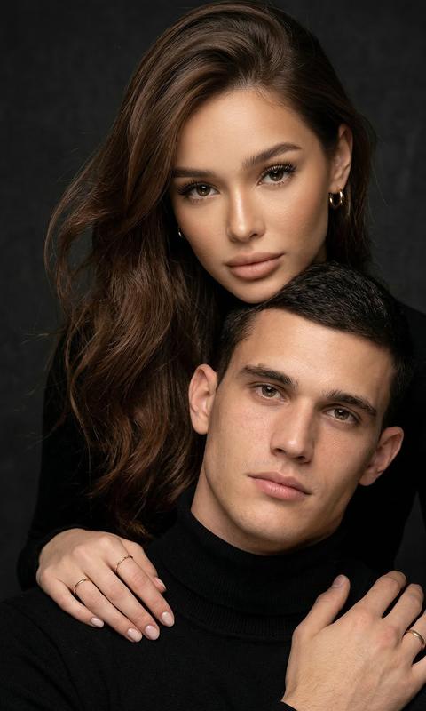 Гиперреалистичный студийный fashion-портрет молодой пары по загруженному референсу, 100% сходство лиц. Крупный план, кадр по плечи.
Мужчина, спокойный уверенный взгляд прямо в камеру, естественное выражение лица, одет в черный трикотажный свитер с высоким воротом.
Женщина с волосами цветом и длиной как на фото, мягкая боковая укладка. Она стоит позади мужчины и нежно обнимает его, ее руки лежат на его плечах. Ее лицо расположено рядом с его лицом, она повернута слегка боком, голова немного наклонена вперед, взгляд направлен прямо в камеру.
У женщины выразительные глаза с длинными густыми черными ресницами, естественный clean-glam макияж, натуральные брови, нюдовые губы, теплый оливковый оттенок кожи, небольшие серьги-кольца.
Композиция плотная и интимная, их лица расположены очень близко друг к другу, современный модный портрет пары.
Кожа максимально натуральная: живая текстура кожи, видимые микропоры, subtle skin glow, естественный мягкий блеск кожи, natural skin microtexture, skin translucency, micro skin details, легкие естественные несовершенства кожи, без ретуши и без эффекта пластика.
Освещение: мягкий студийный beauty lighting, рассеянный ключевой свет спереди и немного сбоку, мягкие глубокие тени для объема лица, деликатные световые блики на коже.
Фон: глубокий темный студийный фон, темно-графитовый или почти черный, создающий контраст с кожей и лицами.
Стиль: luxury fashion editorial photography, high fashion portrait, ultra photorealistic, 85mm portrait lens, shallow depth of field, creamy bokeh, cinematic soft lighting, RAW photo, extremely detailed, fine hair strands, natural skin pores, professional photography, photorealism, 8k, high dynamic range.
Вертикальный формат 9:16
Негативный промт:
ai plastic skin, wax skin, overly smooth skin, doll face, beauty filter, cgi, 3d render, overretouched skin, unrealistic skin texture, bad anatomy, distorted face, extra fingers, low detail, blurry skin, artificial texture, oversharpen, fake lighting