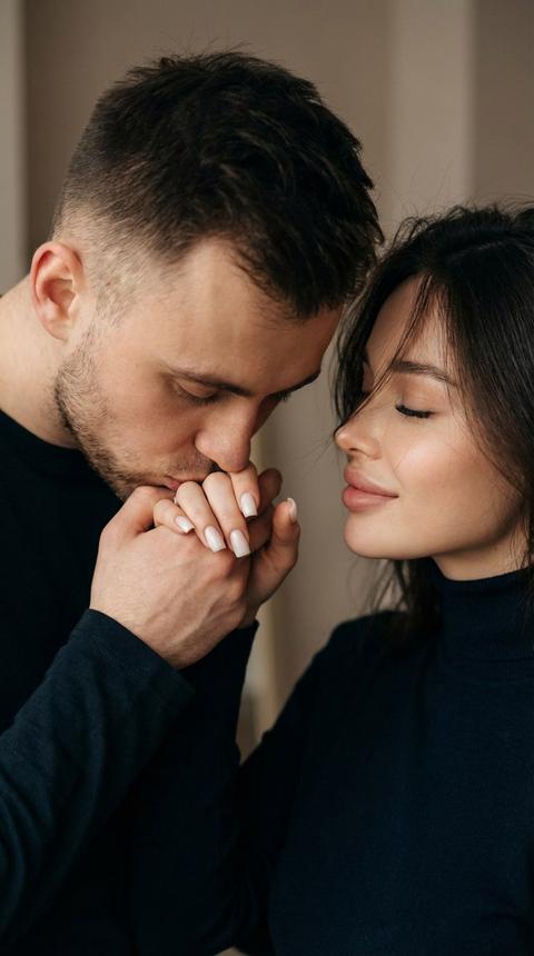 Не меняя внешности людей с фото, изображена интимная сцена глубокой эмоциональной связи между мужчиной и женщиной, снятая в цветной гамме, создающей атмосферу задумчивости и нежности. Их лица находятся очень близко друг к другу, мужчина нежно целует руку женщины, которую она протянула вперёд, словно отдавая мгновение души и доверия. Женщина повернула голову в профиль, её закрытые глаза и лёгкая улыбка выражают покой и внутреннее умиротворение. волосы женщины аккуратно падают вниз, немного прикрывая её лицо, её пальцы изящно обхватывают руку мужчины, что придаёт сцене трогающую реалистичность и близость. Маникюр молочный квадрат. Мужчина согнул руку в локте и наклонился к руке женщины, погружаясь в этот момент с особой концентрацией и уважением. Одеты они в тёмные однотонные вещи с гладкой текстурой, которые не отвлекают от главного – их чувств, подчёркнутых мягким контрастом света и тени, равномерно освещающим их лица и руки. Задний фон нейтрален и размытый, не привлекает внимания и служит естественной сценой для такого трогательного, почти кинематографического кадра, где ощущается тихая интимность и глубокая эмоциональная связь между двумя людьми, что подчёркивается атмосферой, созданной освещением и чётким, детальным изображением их кожи, волос и тонов лица, обеспечивая чувство присутствия и живости момента, фотореалистичное изображение, высокая текстурная детализация, высокое качество, разрешение 8K. 9:16