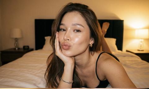 Создай портрет, не меняя черты лица. hyper realistic vertical photo collage, качество съёмки как на iPhone 17 Pro Max, 9:16
тёплая уютная спальня, большая кровать с белым бельём, мягкое изголовье, тёмные стены, на заднем плане размытая прикроватная тумбочка и лампа, фон слегка в боке
молодая девушка,  волнистые волосы, пряди падают на лицо и частично закрывают один глаз, сияющая кожа, безупречный  макияж: подчёркнутые ресницы, ровный тон, золотистый хайлайтер, пухлые глянцевые нюдовые губы, маленькие золотые серьги, серебро браслет на запястье, черная  майка на тонких бретелях
вертикальный коллаж из трёх кадров, вдохновлённый Pinterest, эстетика инстаграм-инфлюенсера:
– верхний кадр: девушка лежит на кровати на животе, опирается щекой на ладонь, локоть на подушке, смотрит прямо в камеру, делает «duck face» губами, ракурс немного сверху и чуть ближе, кадр по грудь, фон кровати размыт
– средний кадр: экстремальный крупный план лица и губ, фокус на блестящих губах и браслете на руке, девушка слегка высовывает язык и прикусывает его, рука лежит поперёк кадра, браслет даёт яркий блик, фон и остальное лицо сильно в боке
– нижний кадр: девушка лежит боком на кровати, голова на согнутой руке, волосы растрёпаны по подушке, она смотрит в камеру расслабленным, немного томным взглядом, лёгкая улыбка губами, ракурс чуть сверху, видна линия плеч и часть тела
свет: тёплый жёлто-оранжевый свет как в гостиничном номере, сочетание мягкого комнатного света и прямой вспышки смартфона, яркие блики на коже и губах, контрастные тени позади, подчёркнутый влажный блеск кожи
обработка: стильные Pinterest-пресеты, тёплый оттенок, повышенная контрастность, лёгкое виньетирование по краям, мягкий цифровой шум и лёгкая плёночная зернистость, сохраняется текстура кожи и поры без чрезмерного сглаживания, гладкие глянцевые губы, насыщенные тёплые тона, слегка приглушённый фон
супер детализировано, фокус на лице и губах, реалистичная кожа, cinematic, pinterest aesthetic, instagram model, shot on iphone 17 pro max, HDR, high resolution