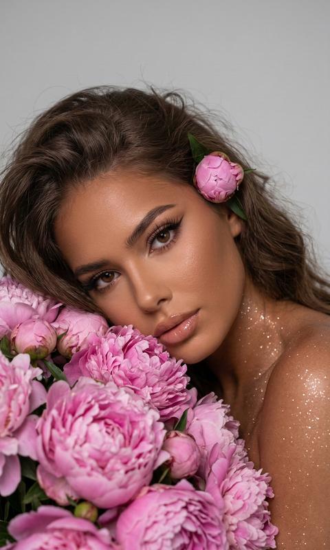 Не меняй черты лица 
Крупный план женщины с слегка растрёпанными волосами объемными красивыми , которая лежит на боку, прижавшись к обильному, яркому букету цветущих розовых пионов \. Ракурс немного сверху, взгляд модели направлен прямо в камеру\.Мягкий, рассеянный студийный свет нежно подчёркивает влажный блеск её губ на которые нанесён нюдовый блеск, и загар\. На теле много блестящего шиммера , на глазах стрелки и аккуратные реснички с удлиненными уголками лисий эффект  \.Фон однотонный, светло\-серый Глубина резкости очень мала: глаза женщины и ближайшие цветы идеально чёткие, в то время как задний план и некоторые дальние части букета мягко размыты что усиливает ощущение интимности и изолирует объект съёмки, придавая кадру мечтательное, художественное качество\. Общее настроение — чувственное, уязвимое, элегантное и свежее, напоминающее кадр из высокобюджетного рекламного ролика парфюмерии или обложку модного журнала\.
Высокая детализация кожи и цветов\. 
За ухом у девушки розовый пион\.
Вертикальное изображение\.
9:16
