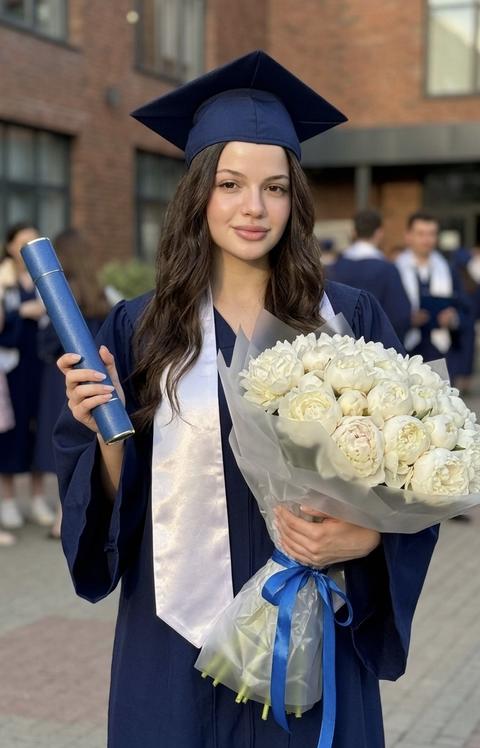 Загруженное изображение - эталон . Молодая девушка на фото. привлекательной и изысканной атмосферой в эстетике Pinterest. 
Фотореализм , снято на 17pro max IPhone.Не меняя внешности женщины с фото, в центре композиции предстает молодая выпускница в классической манте насыщенного темно-синего цвета, переливающейся в жарких лучах вечернего солнца, головной убор – квадратная академическая шапка – придает образу официальность и торжественность. Её грудь украшает перламутрово-белый атласный шарф, мягко отражающий свет, создавая игру бликов и теней на гладкой поверхности ткани. В правой руке она уверенно держит синие документы с едва заметным принтом, зажатые аккуратно, что подчеркивает важность момента. Левая рука преподносит объемный очень большой букет, состоящий из белоснежных пионов с нежными бутонами, упакованных в тонкую, слегка прозрачную оберточную бумагу с атласной синей лентой, добавляющей композиции изящества и легкости. Лицо девушки выражает спокойствие и мягкую гордость, на лице мягкая полуулыбка.с аккуратно уложенными очень длинными волнистыми волосами, свободно спадающими по плечам и слегка обрамляющими лицо, усиливая его естественную красоту и отражение теплого солнечного света. Фон дополнен универской атмосферой — кирпичные фасады зданий плавно уходят в перспективу, на них падает дневной свет, рассеиваясь и создавая мягкие тени. За девушкой видны размытые силуэты прохожих, что придает сцены живость и динамику, не отвлекая от главного героя. Вся сцена наполнена ощущением торжественного завершения и нового начала, подчеркивая важность момента празднования и достижения цели с гармонией и элегантностью, фотореалистичное изображение, высокая текстурная детализация, высокое качество, разрешение 8K.
Кожа женщины реалистична, не выдает ai эффектов, ее кожа выглядит естественно, с ровным, здоровым тоном и эффектом влажного сияния
Гиперреализм , высокая контрастность 
Фото во весь рост!