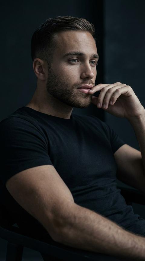 Создай портрет, не меняя черты лица. Крупный план молодого мужчины . У него выразительные глаза и задумчивый взгляд. Он одет в простую черную облегающую футболку. Мужчина сидит в расслабленной позе, одна рука поднесена к лицу, пальцы слегка касаются губ. Освещение мягкое, драматичное, в стиле «low-key», создающее глубокие тени и подчеркивающее рельеф лица и мышц. Фон темный, минималистичный, размытый. Цветовая гамма приглушенная, в холодных кинематографических тонах. Высокая детализация кожи и текстуры волос, профессиональная студийная фотография.
Muted cool tones, hyper-realistic skin texture, 8k resolution, shot on 85mm lens, studio photography.