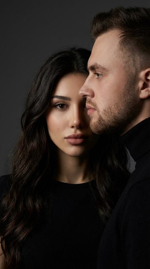 Создай портрет, не меняя черты лица. студийный портрет женщины и мужчины, стоящих чрезвычайно близко друг к другу; их лица выровнены по одной вертикальной оси, создавая драматичную композицию с перекрытием половин лица.Женщина с волнистыми длинными волосами, смотрит прямо в камеру спокойный, интенсивный и уверенный взгляд.
Мужчина находится в строгом боковом профиле, повернут к женщине и частично перекрывает её лицо.Минималистичный тёмный студийный фон, плавный серый градиентный бэкграунд.Оба одеты в чёрные минималистичные образы:женщина в матовом чёрном топе,мужчина в чёрной водолазке
Свет: кинематографичное освещение в стиле Рембрандта — мягкий ключевой свет слева от камеры, освещающий лицо женщины; тонкий контровой свет подчёркивает профиль мужчины; глубокие тени.
Настроение: таинственное, мощное, интимное, эстетика люксовой журнальной обложки.