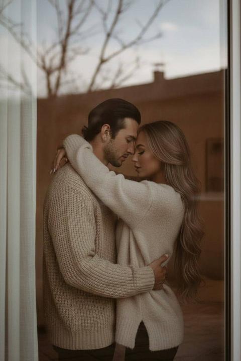 Используйте внешность пользователей 1:1 — лица, кожу, волосы и черты не менять. Создай тёплый, ультрареалистичный портрет пары, стоящей очень близко друг к другу в уютной комнате, словно в мягких объятиях. Мужчина в бежевом вязаном свитере нежно держит женщину, а она — в мягком бежевом свитере, обнимает его за шею, наклоняясь ближе. Камера как будто снимает их через большое окно снаружи: стекло даёт лёгкие отражения неба и ветвей деревьев, создаёт атмосферу глубины и интимности. Естественный дневной свет мягко подсвечивает их лица и контуры, добавляя спокойное сияние. Лёгкое размытие и блики на стекле усиливают ощущение приватного момента, будто пойманного случайно. Высокая детализация, кинематографичность, мягкие тени, минималистичная палитра бежевых и нейтральных оттенков. Профессиональная, фотореалистичная съёмка крупным планом.