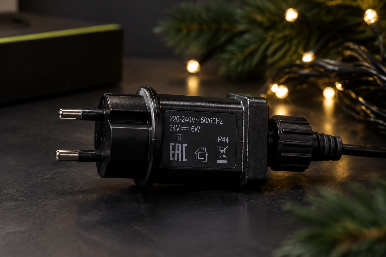 Крупный план вилки адаптера питания новогодней гирлянды (220V на 24V), на корпусе четко видна маркировка знака EAC, пара